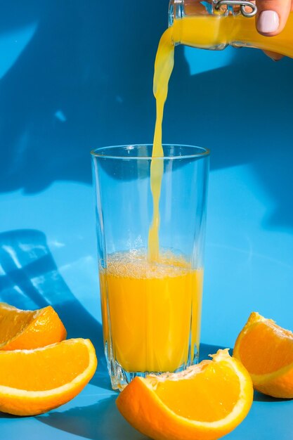 Pouring orange juice stream from jug into glass of squeezing orange juice with sliced fruits