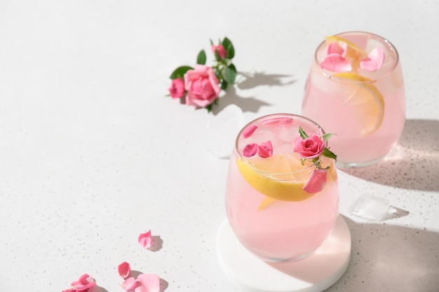 Pouring pink alcoholic cocktail with rose flowers on white background