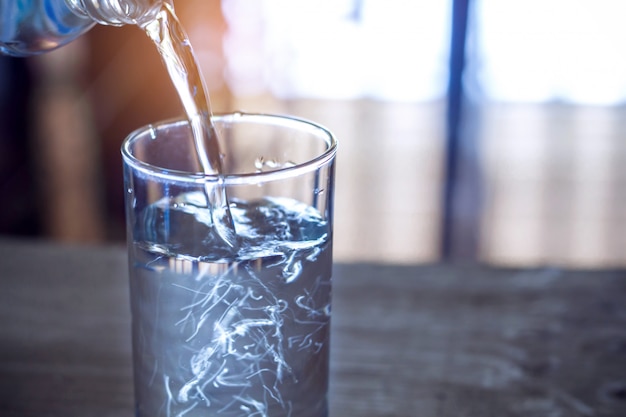 Foto acqua purificata della bevanda fresca di versamento dalla bottiglia sul fondo di vetro della tavola