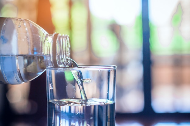 Pouring purified fresh drink water from bottle on glass table background