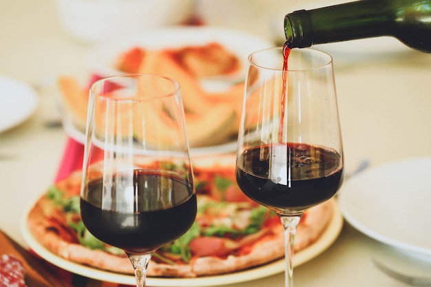 Pouring red wine from bottle into  glasses on table with food background