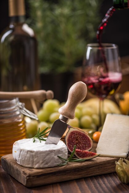 Photo pouring red wine into glass and serving with camembert