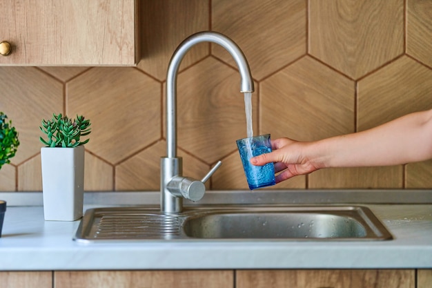 Pouring running purified filtered tap water in glass at kitchen for healthy drinking