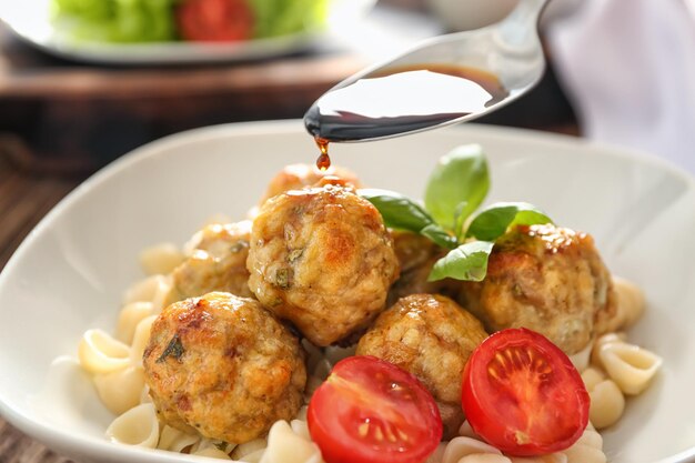 Photo pouring tasty sauce into bowl with turkey meatballs and pasta closeup