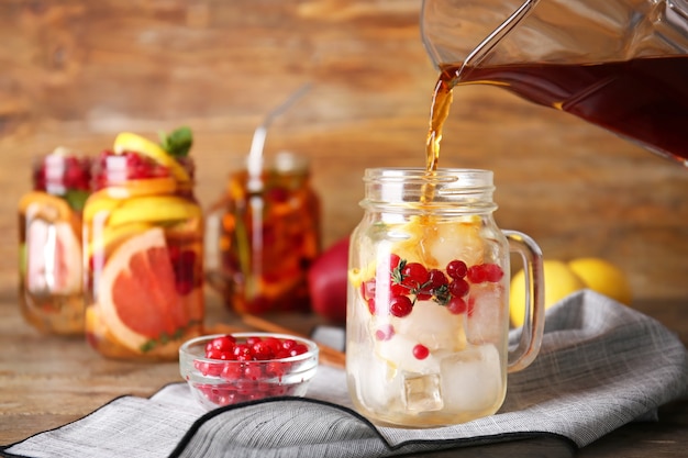 Pouring of tasty tea into mason jar on table