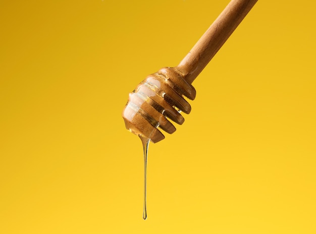 Pouring transparent sweet honey from a wooden stick. Yellow background. Food levitates