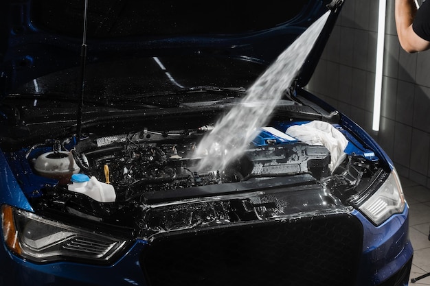Поливание водой двигателя автомобиля Мойка двигателя автомобиля щеткой-распылителем и моющим средством в автосервисе Детализация очистки двигателя от пыли и грязи