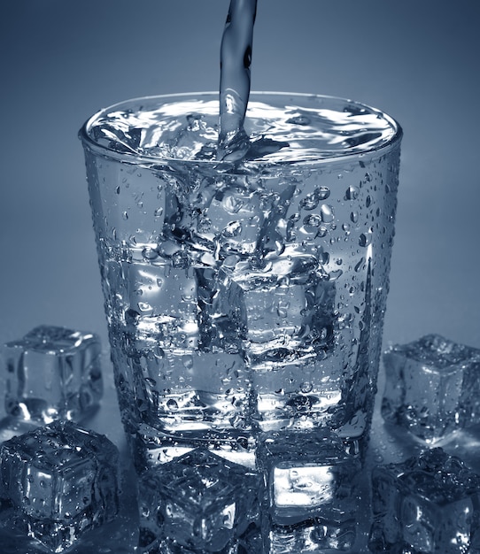Pouring water drink into glass with ice cube