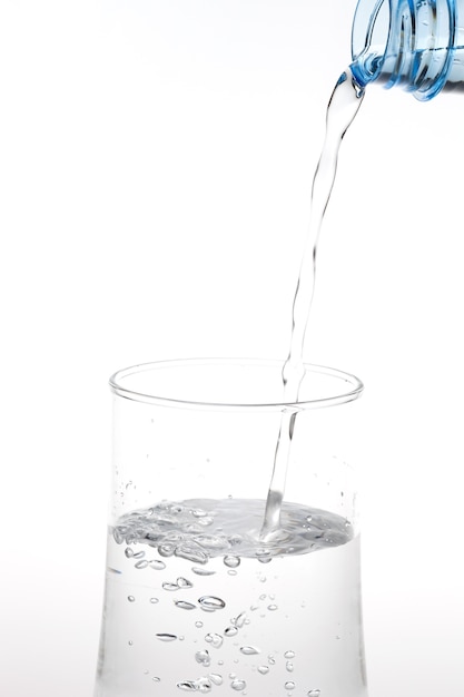 Pouring water from bottle into glass on white background.