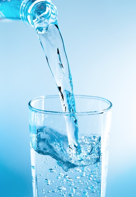 Pouring water from bottle into glass with blue light