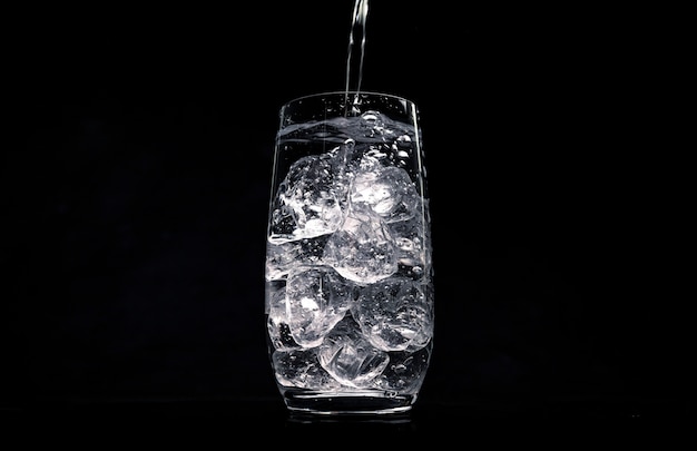 Pouring water in glass with crushed ice on black space