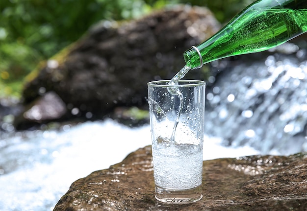 写真 小さな滝の背景にカップに水を注ぐ