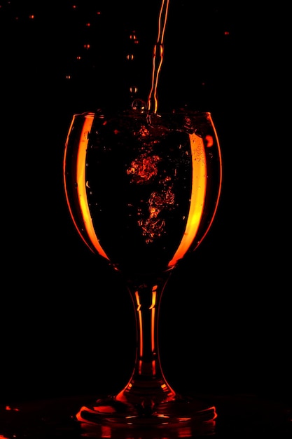 Pouring water into a glass on black background. Orange water in a glass