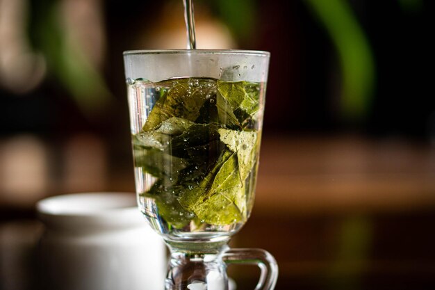 Foto versare l'acqua in un bicchiere di vetro con le foglie secche