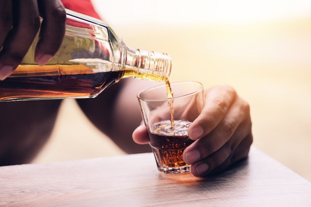 Pouring whiskey or alcohol drink from bottle to glasses on wooden  Pour liquor 