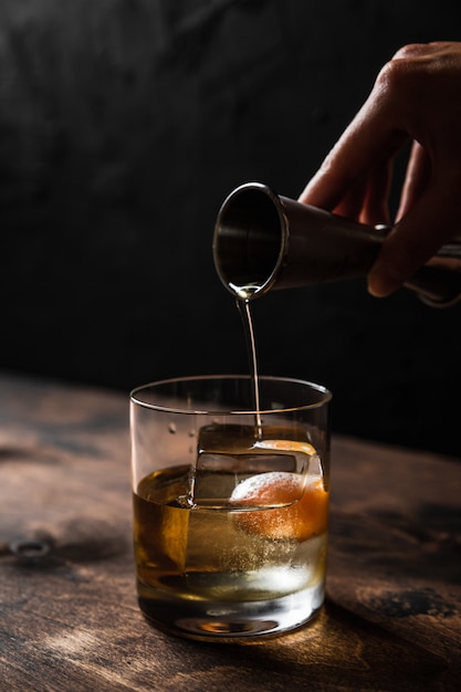 Pouring whisky from a jigger into a rocks glass with a big ice cube, back light