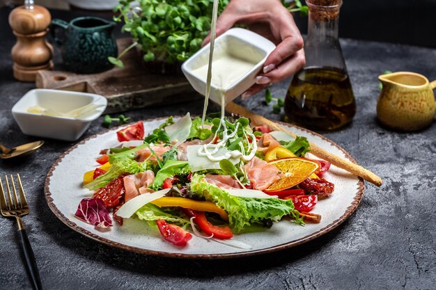 Pouring white sauce over plate of cooked salad with pieces of smoked salmon, lettuce, sun dried tomatoes and herbs, Healthy food. Dietary menu,