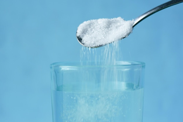 Pouring white sugar in a glass of water on table