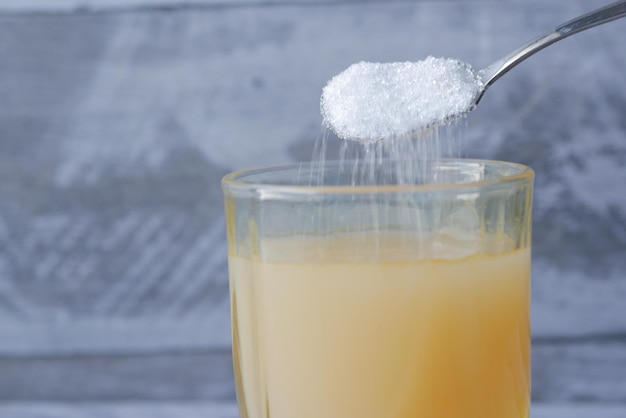 Pouring white sugar in a glass of water on table