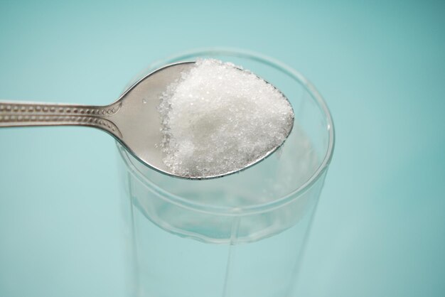 Pouring white sugar in a glass of water on table