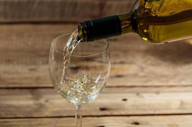 Pouring white wine in a glass on wooden background