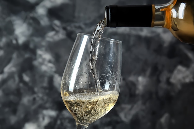 Pouring of wine from bottle into glass on grey surface