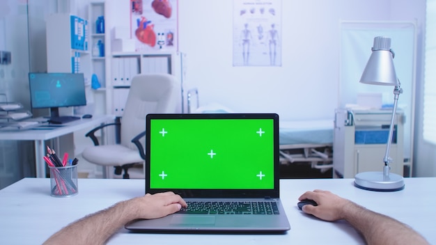 Pov of assistant using laptop with copy space available in hospital cabinet and doctor working on computer. Medic using notebook with chroma key on display in medical clinic.