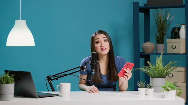 POV of content creator reading comments on camera, answering questions with smartphone. Female vlogger filming video for social media channel, using mobile phone. Tripod shot.