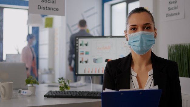 Pov di imprenditore che parla con il team mentre scrive informazioni aziendali durante la riunione di videochiamata online in ufficio. libero professionista che indossa una maschera protettiva per prevenire l'infezione da coronavirus