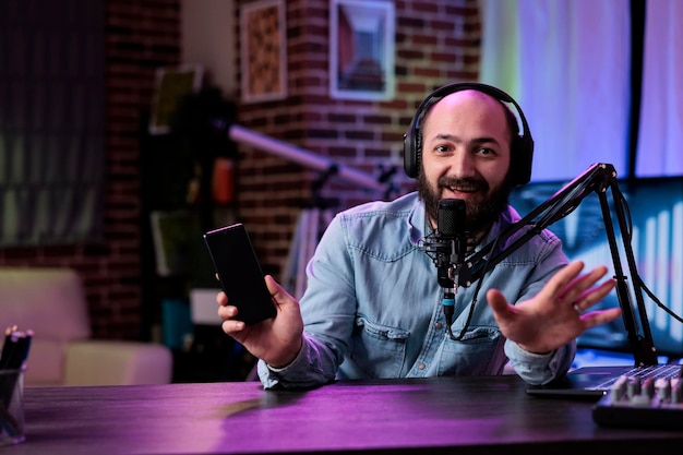 POV of male lifestyle vlogger recommending mobile telephone on podcast, broadcasting live video on social media channel. Cheerful man doing product review with modern smartphone on camera.