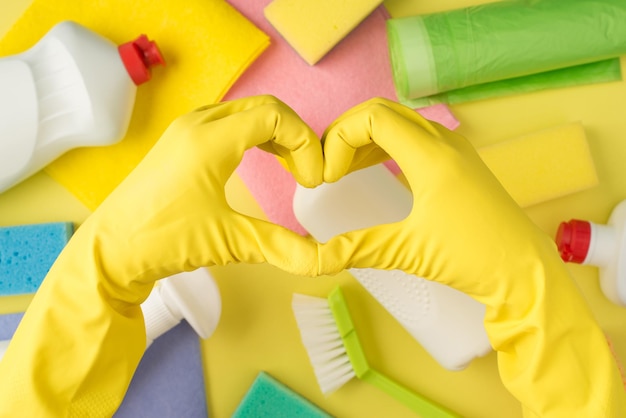 Above pov photo of equipment for cleaning and hands in yellow gloves with gesture as heart isolated on the yellow background