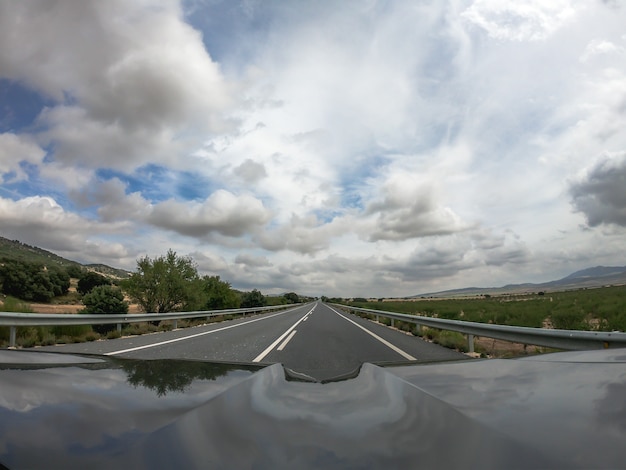 Pov rijdt in een zwarte auto op een tweerichtingsasfaltweg met uitzicht op het platteland in Andalusië met verspreide en lage wolken, een boomplantage. Niet inhalen signaal. Een hoogspanningslijn steekt de baan over.