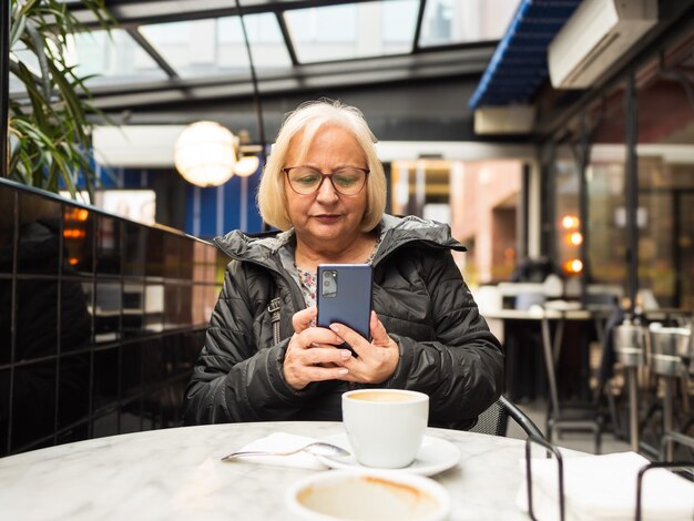 Foto pov senior vrouw kijkt naar mobiele telefoon met koffie al klaar