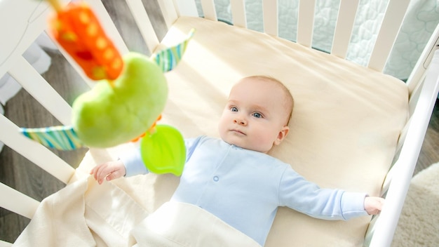 Photo pov of shaking toy and looking at little baby boy lying in cradle at bedroom concept of parenting family happiness and baby development