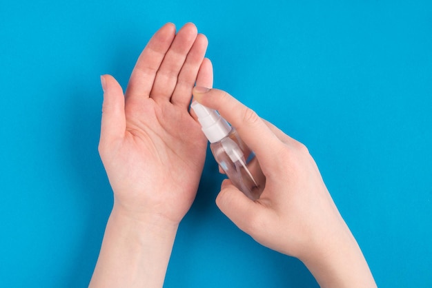 Pov top overhead close up sopra vista foto di mani femminili usando l'applicazione di spray da una piccola bottiglia sulle mani isolate su uno sfondo blu di colore brillante