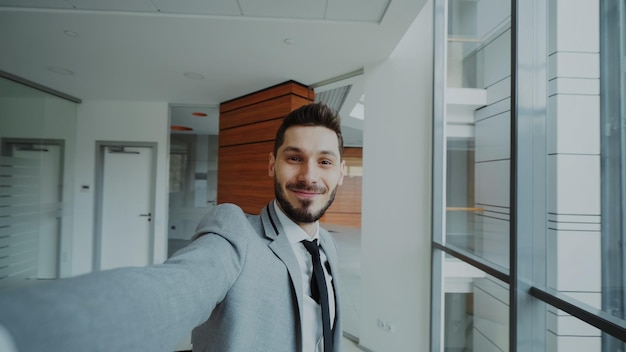 POV van een jonge zakenman in pak die een selfie-foto maakt en plezier heeft in een modern kantoor