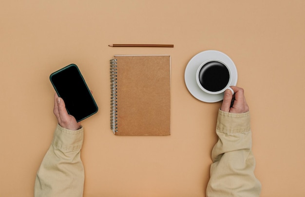 Foto vista pov sulle mani femminili con lo smartphone accanto al taccuino e alla tazza di caffè su sfondo marrone