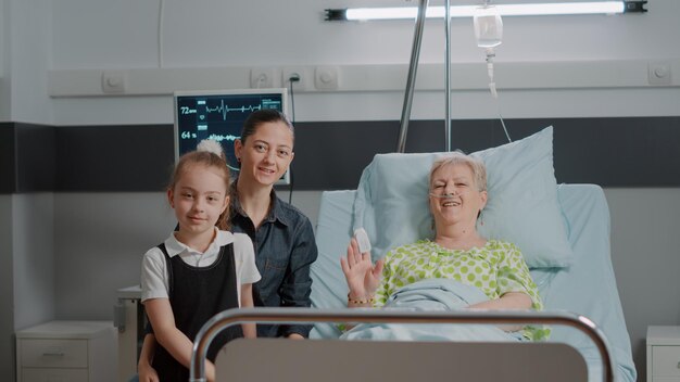 POV of woman and kid using video call conference in hospital ward with aged patient. Family talking on online remote videoconference for telecommunication. Teleconference and telemedicine