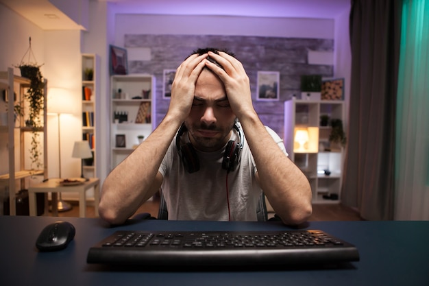 Photo pov of young man covering his face with his hands after losing at online shooter game.