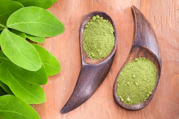 Powder and moringa leaves in bowl on wooden background