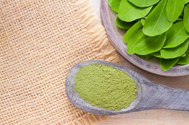 Powder and moringa leaves in bowl on wooden background