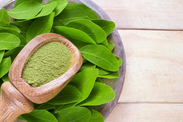 Foto polvere e foglie di moringa in una ciotola su fondo di legno