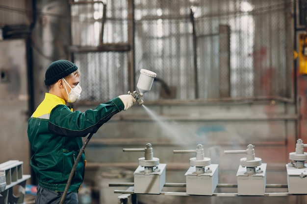 Powder primer coating of metal parts worker man in a protective
suit sprays powder paint from gun on metal product construction at
factory plant