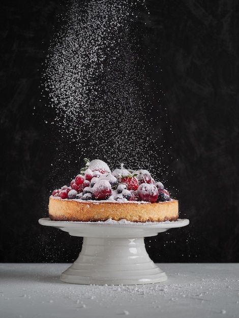 Powdered icing sugar sprinkled on black background on top of\
fresh fruit in a cheesecake