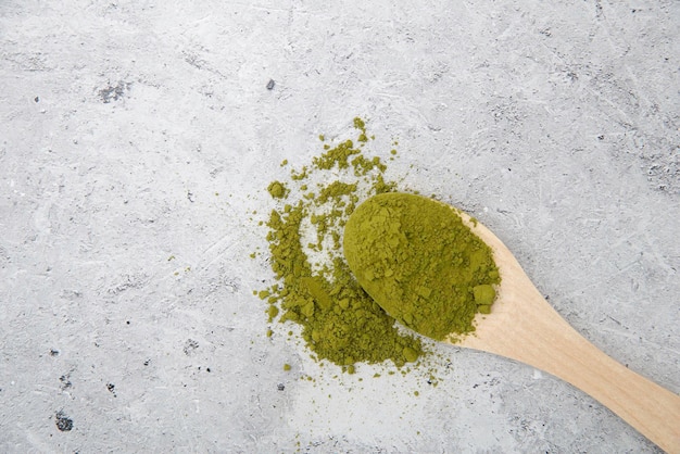 Foto tè verde matcha in polvere in un cucchiaio di legno su un tavolo grigio