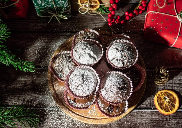 Photo powdered sugar muffins on wooden plate and christmas gifts new year boxes with kraft red green paper decoration