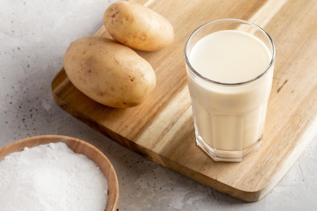 Powdered vegan potato milk glass potato powder and tubers on concrete backdrop Close up