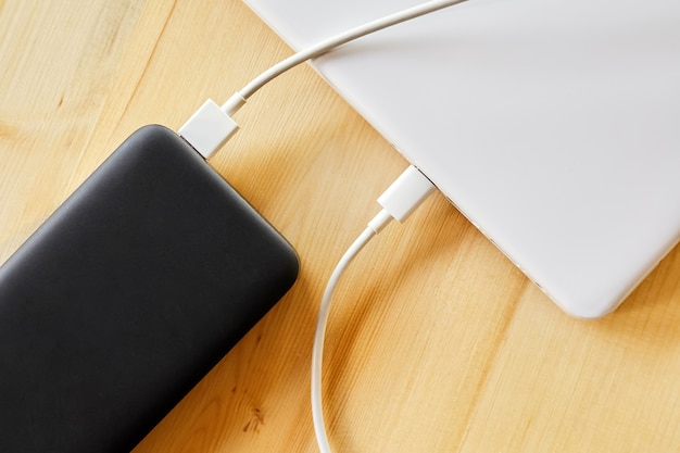 Power bank charges a laptop via USB type C cable on wooden background