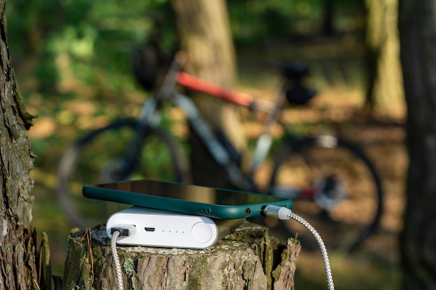 Power bank заряжает смартфон в лесу на фоне велосипеда.