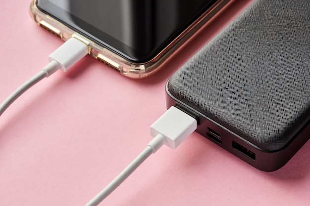 Power bank charges smartphone using a USB cable on a pink surface